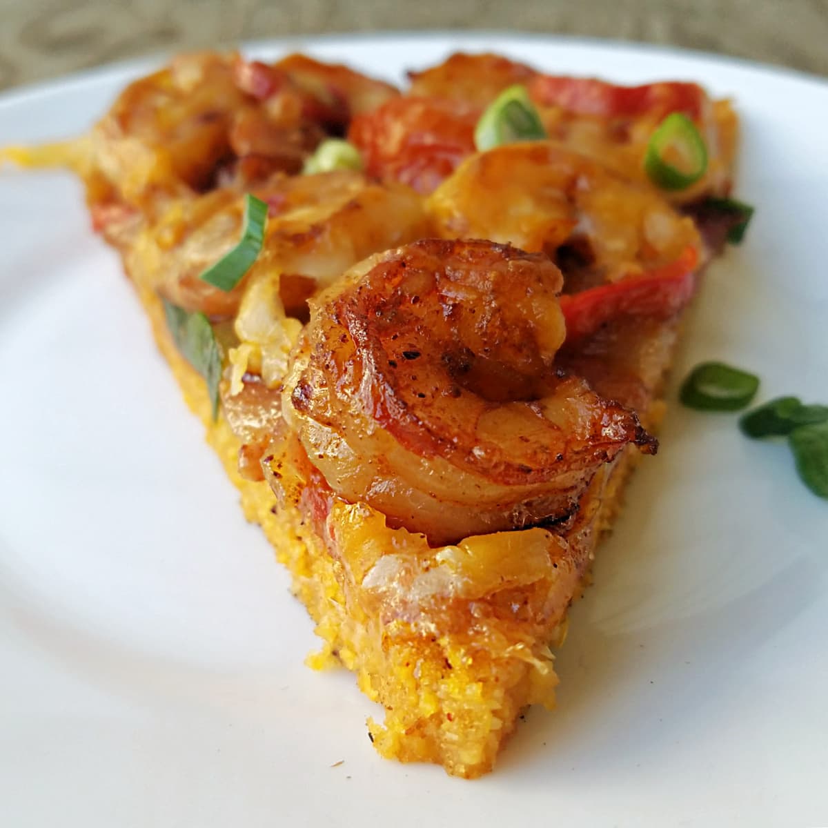 Closeup of single slice of shrimp and grits pizza, point forward. Large shrimp in on the end of the pizza slice. 