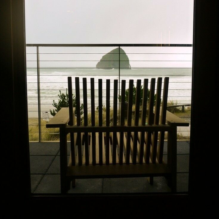 Wooden deck chair from behind, overlooking Haystack rock and a misty ocean. 