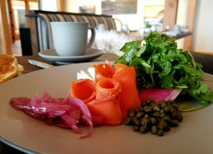 Rolled lox, pickled onions, arugula greens, and capers on beige plate at Meridian. Grey coffee cup in background. 