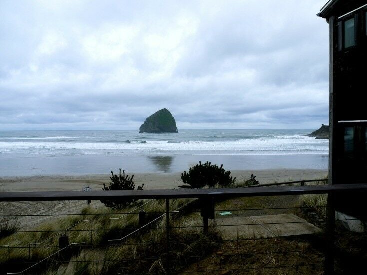 Metal railing, Haystack Rock in distance, with overcast, midday ocean. 