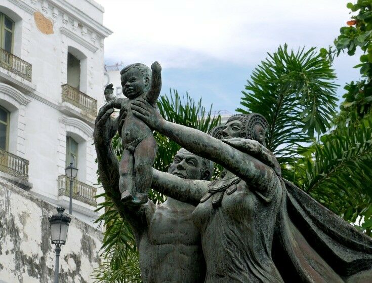 Statue of a man and woman holding a baby aloft. 