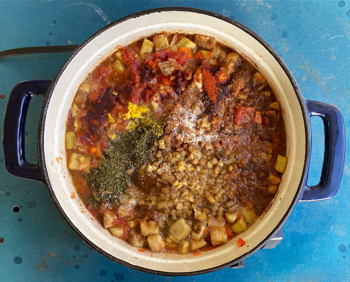 Stew ingredients, including spices and herbs, in a large cast iron Dutch oven.