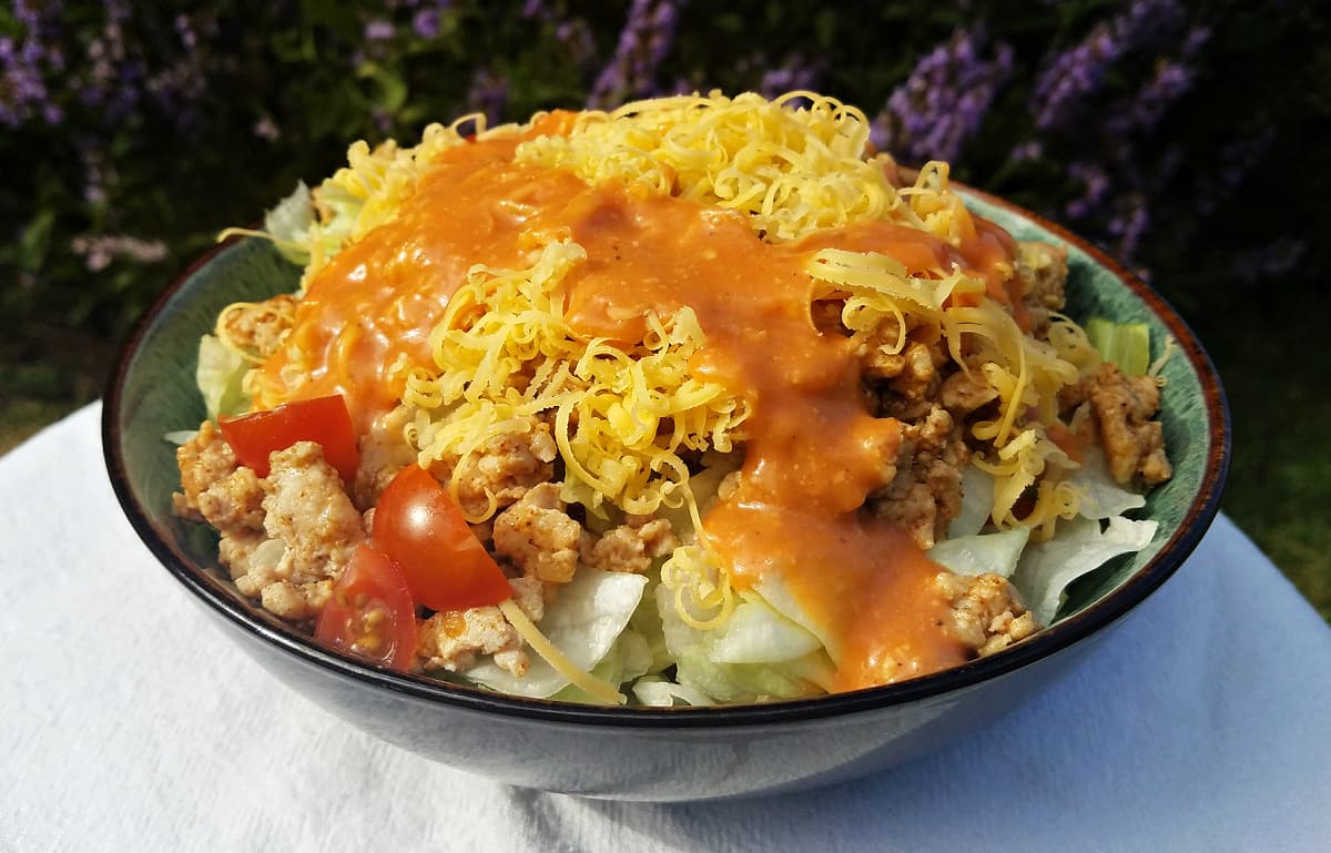 Bowl of salad with grated cheese, tomatoes, ground meat, and creamy french-type dressing on top.
