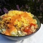 Bowl of salad with grated cheese, tomatoes, ground meat, and salad dressing.