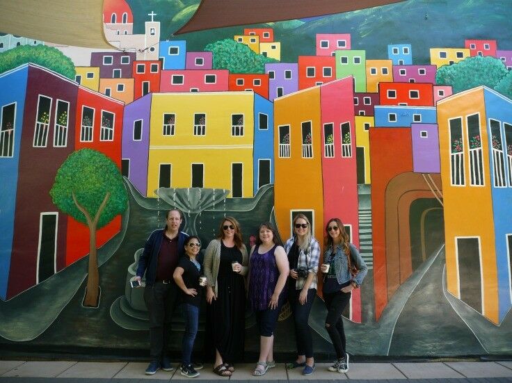 Travel Oregon writers group, standing in front of a large, brightly painted wall mural. 