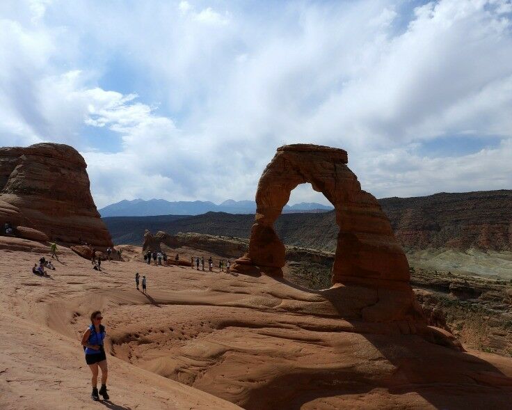 People in the distance near the base of a large sandstone arch. 