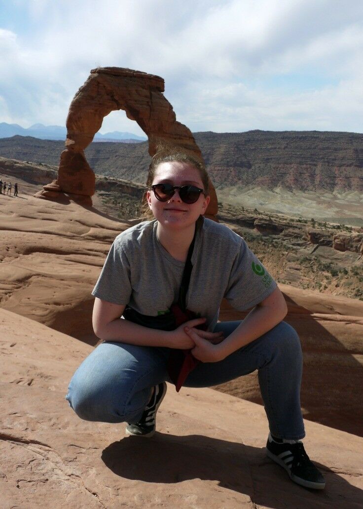 Our Em, wearing sunglasses and smiling, with the Delicate Arch in the background. 