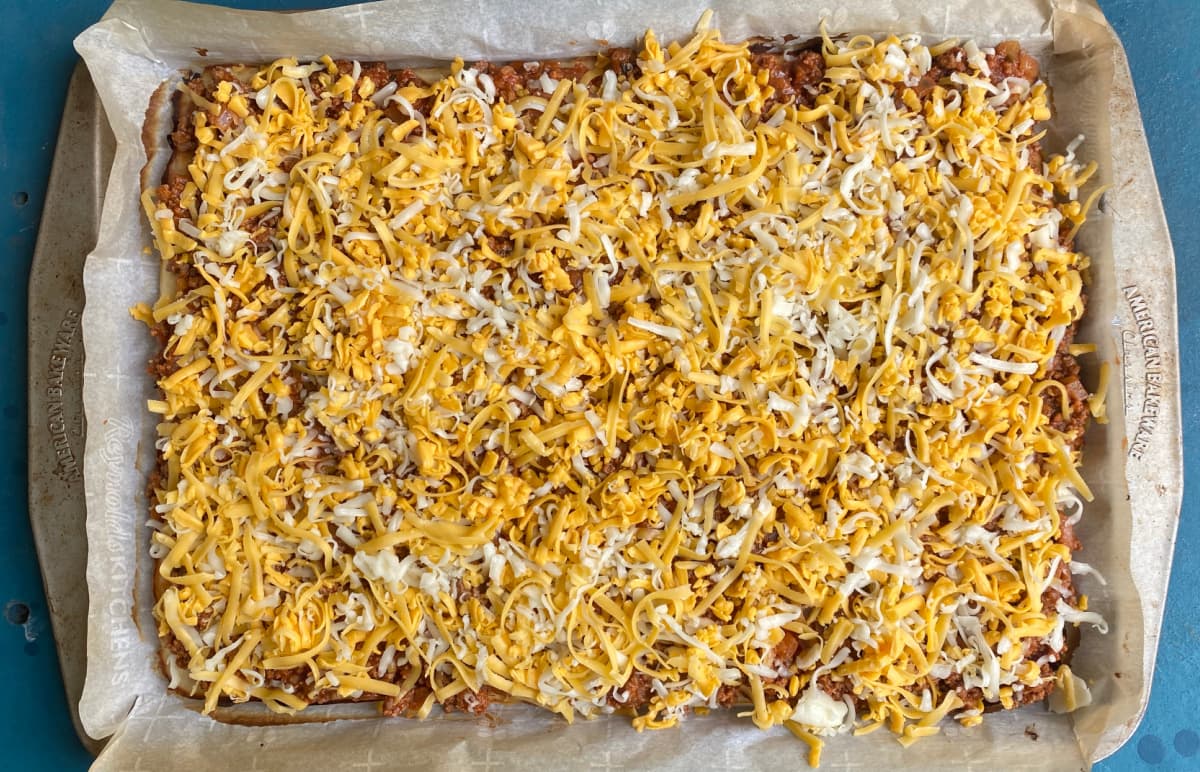 Parbaked pizza crust topped with meat sauce and cheese, ready to bake.