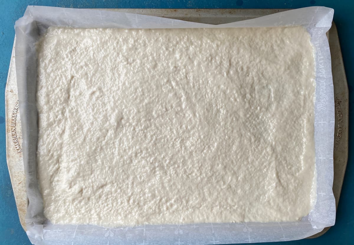 Pizza dough poured onto parchment lined baking sheet.