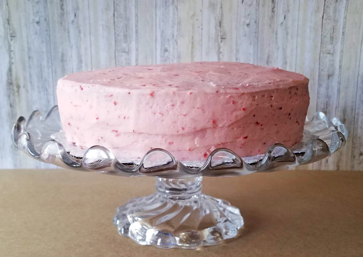 Frosted strawberry cake on glass cake stand.