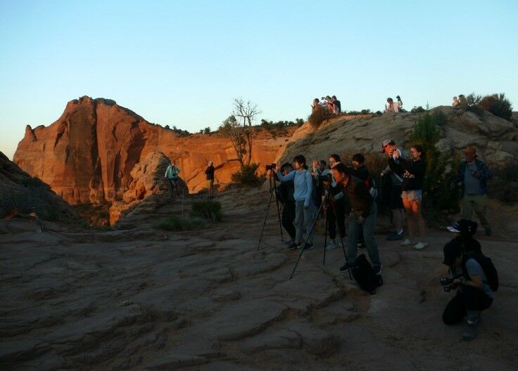 Group of people with cameras on tripods taking pictures of the sunrise. 