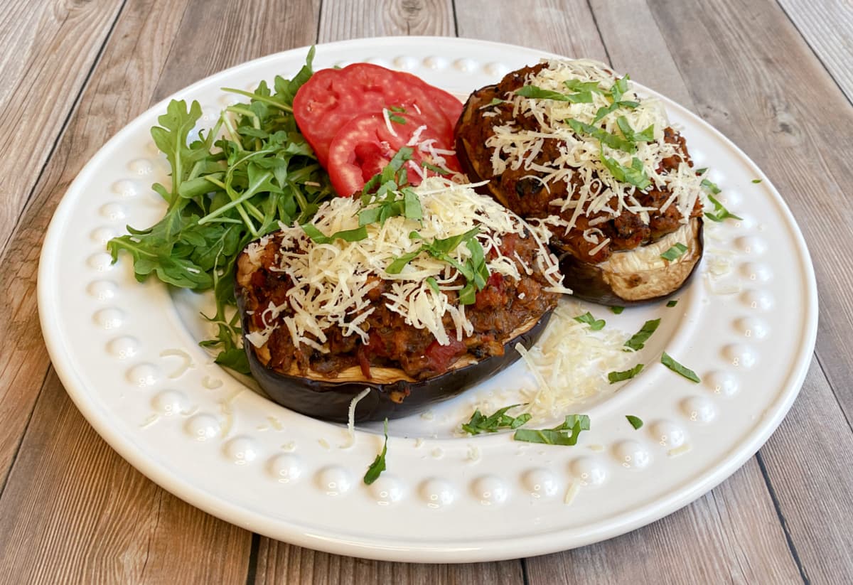 Plate with two baked eggplant boats, garnished generously with parmesan cheese. arugula and tomato salad to the side.