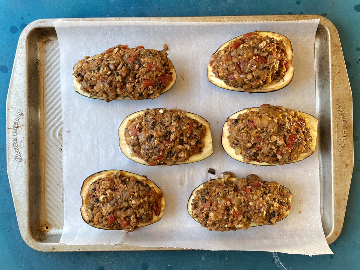 six eggplant halves, stuffes and resting on parchment on a baking tray.