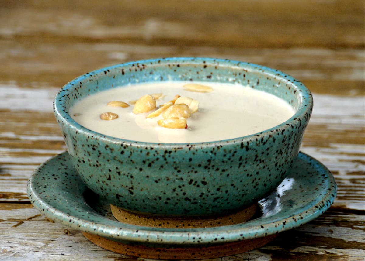 Side view of pottery bowl filled with peanut soup, garnished with peanuts.