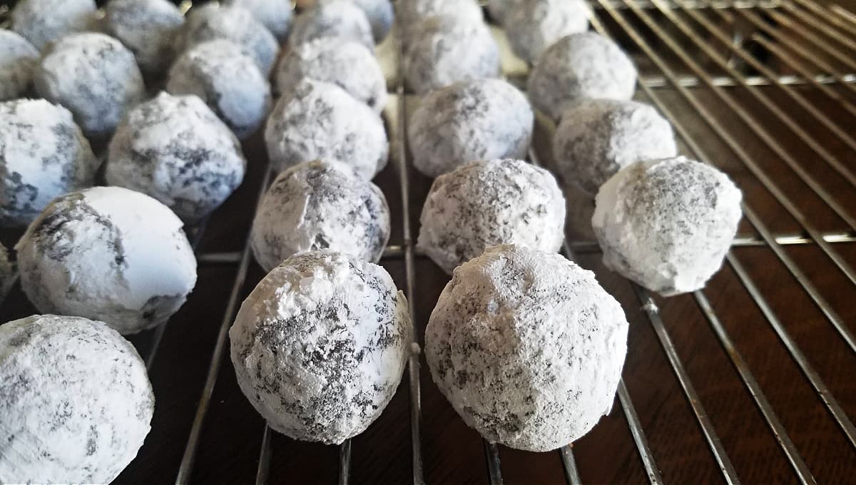 Balls of cookie dough covered with powdered sugar resting on a cooling rack.