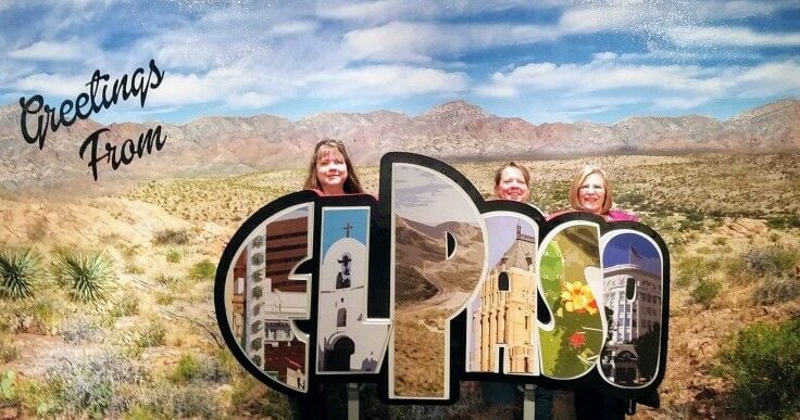 Three friends standing behind the "Greetings From El Paso" postcard photo op at the Museum of Hisory