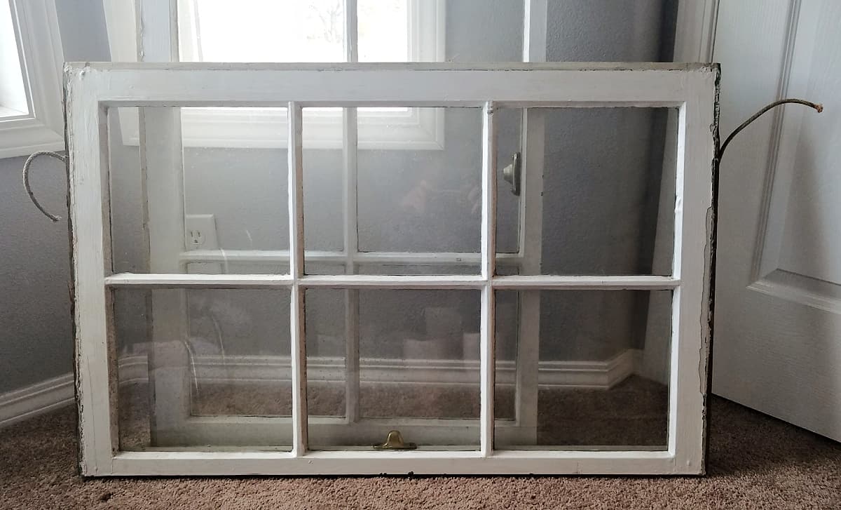 Two dusty old window frames, each with six panels, leaning against a wall.