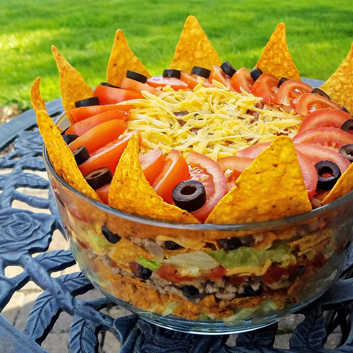 Layered taco sald in a large glass serving bowl, sitting on a wrought-iron bistro table. 