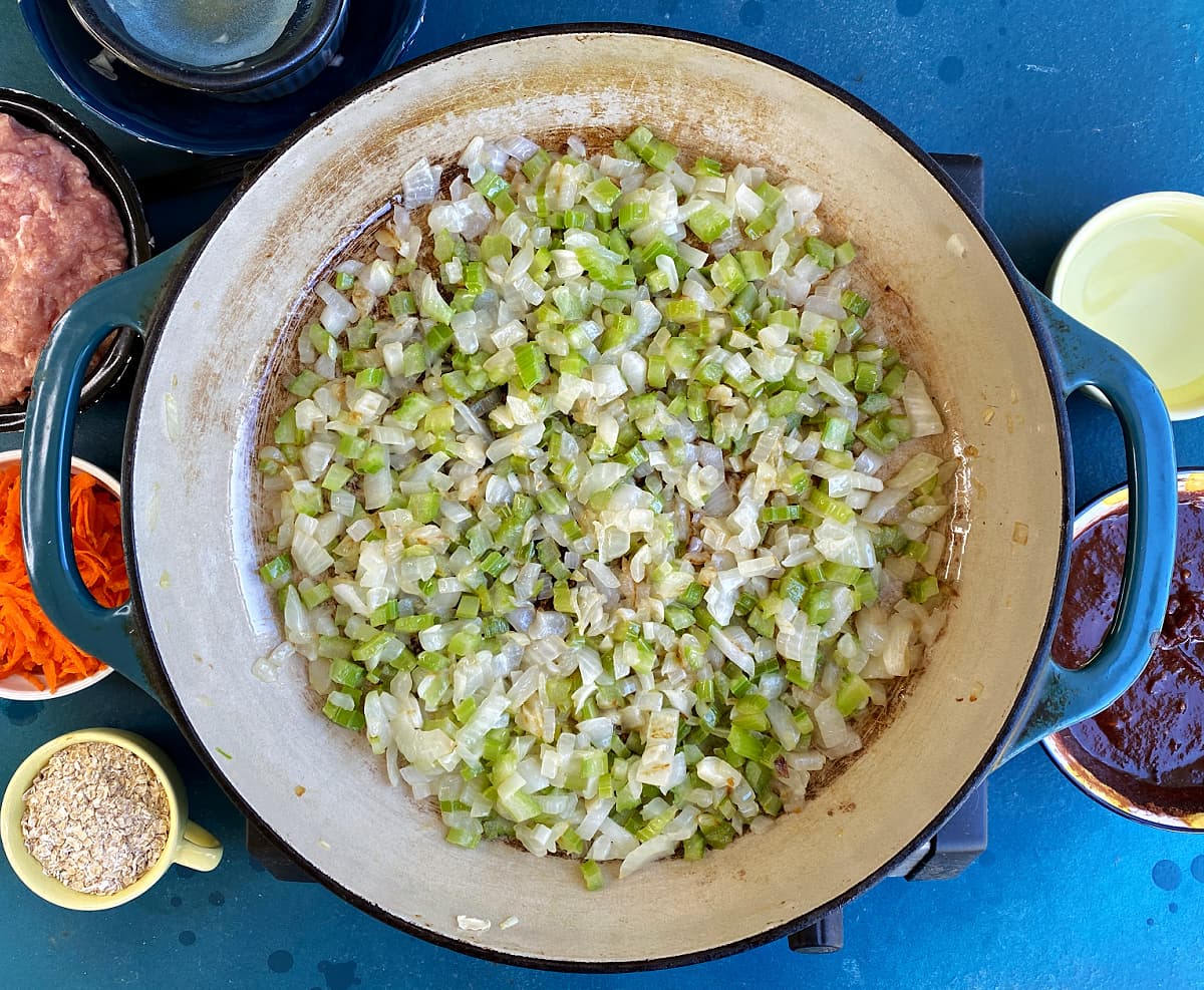 Celery and onion being cooked in a large skillet.