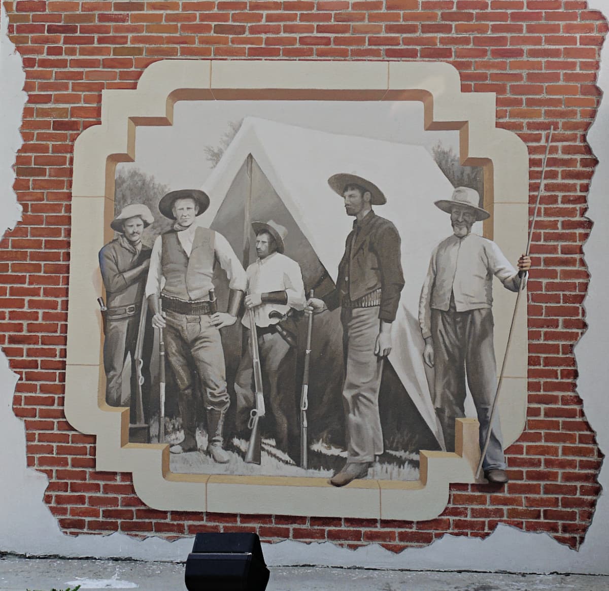 Mural of cowboys in front of a canvas tent, painted in the style of an old-timey photo.