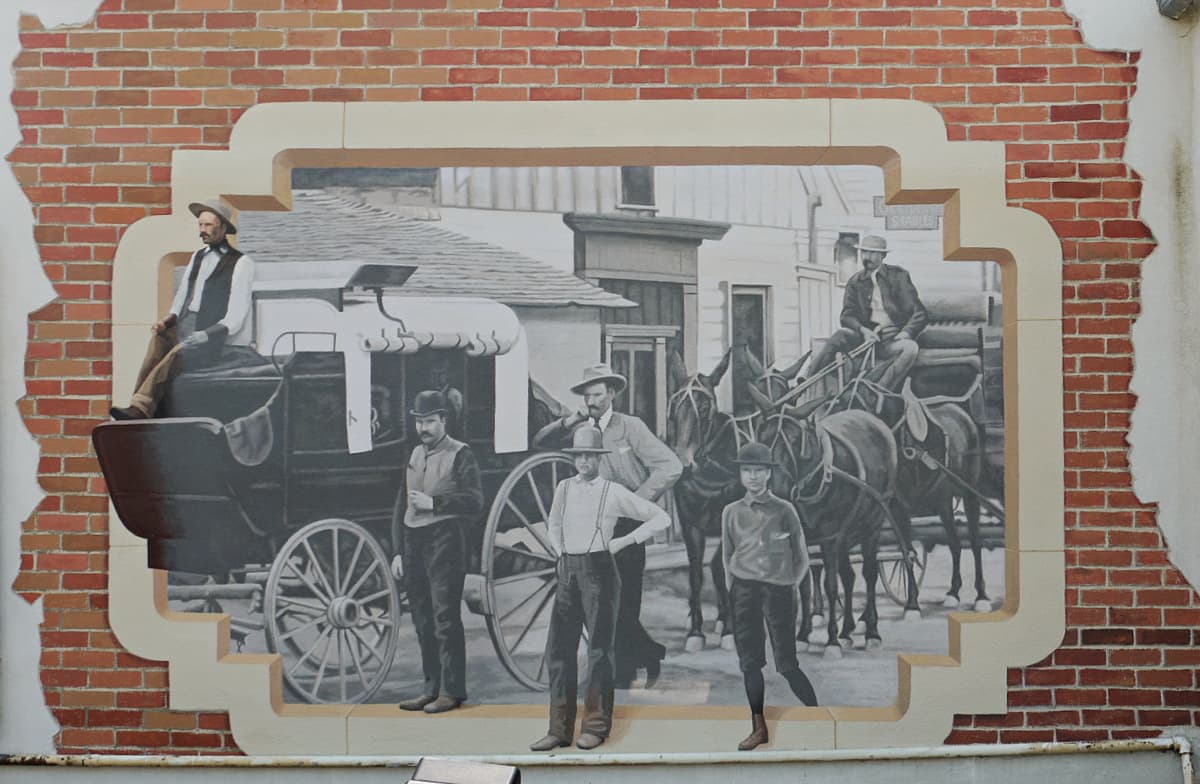 Mural of men in front of an stage coach, painted in the style of an old-timey photo. 