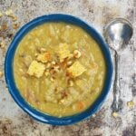 Split pea soup in a blue pottery bowl, sitting on a weather pice of metal. Ornate spoon to the side.