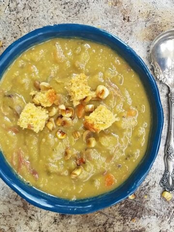 Split pea soup in a blue pottery bowl, sitting on a weather pice of metal. Ornate spoon to the side.
