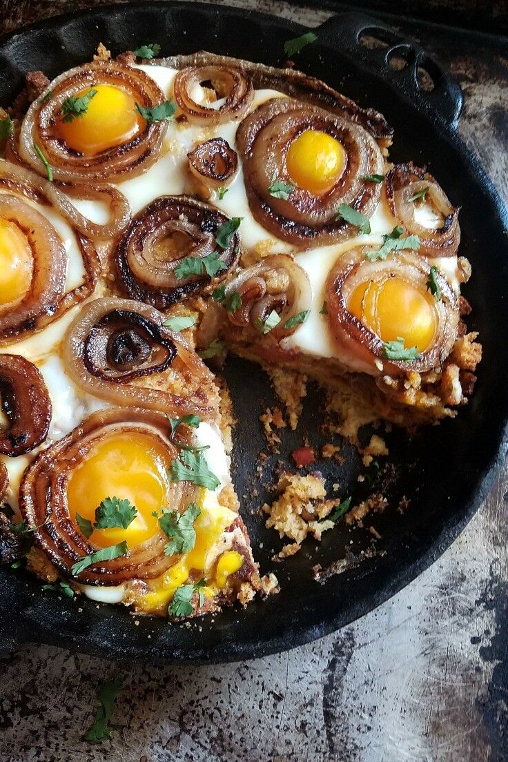 Casserole in cast iron pan, topped with baked eggs and swirly fried onions. 