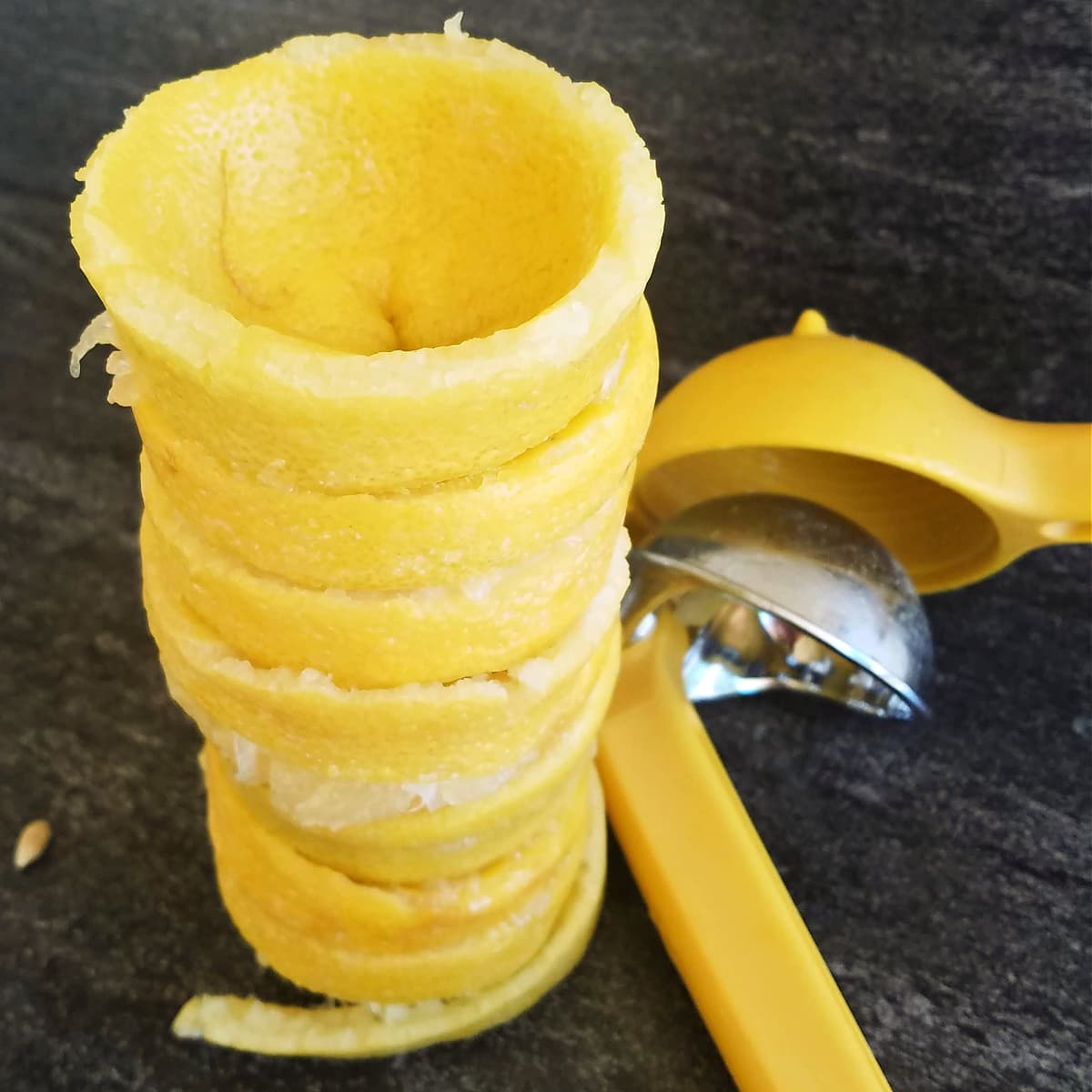Stack of empty lemon rinds next to a lemon squeezer.
