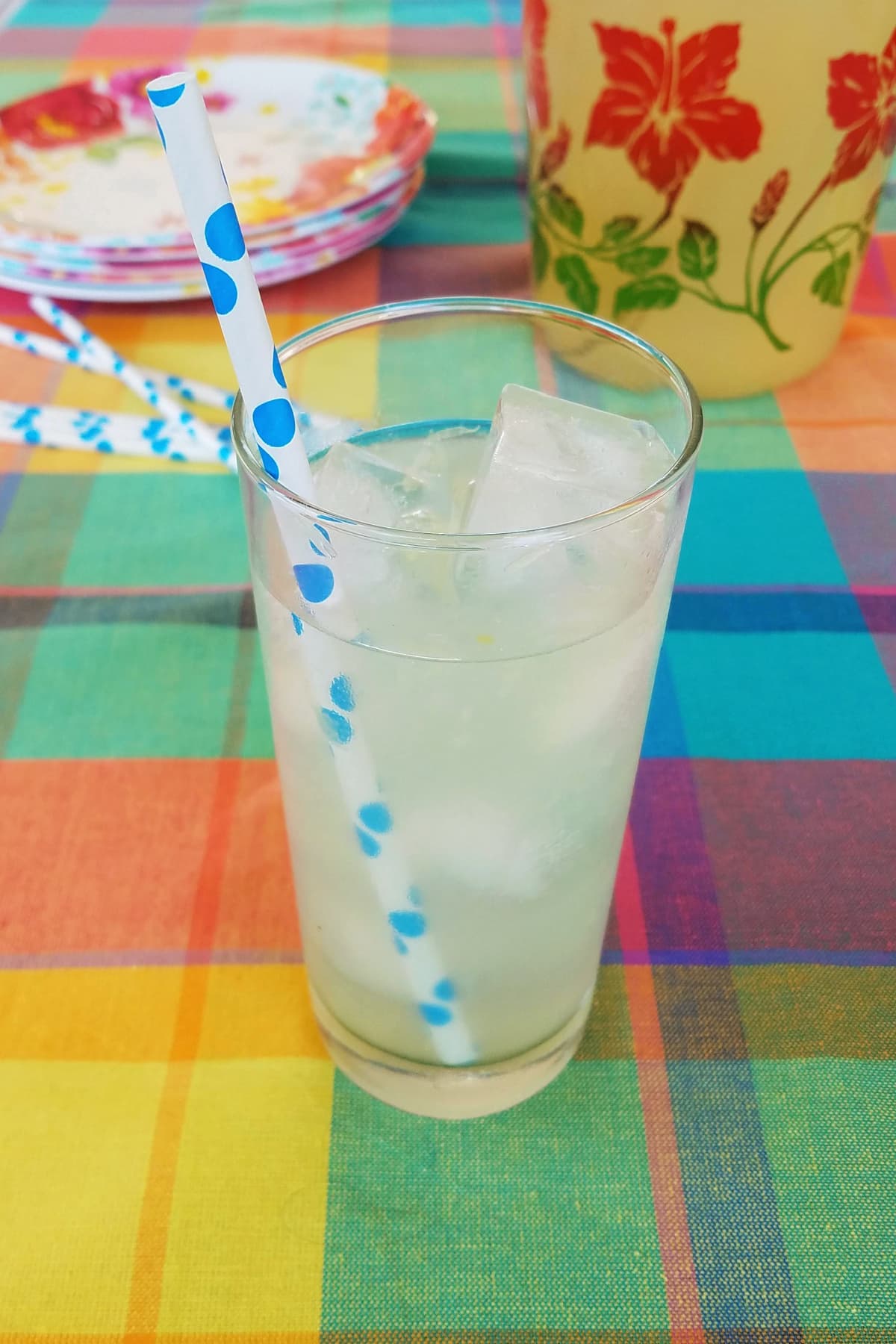 Glass of lemonade with a straw on a table with summery plates.