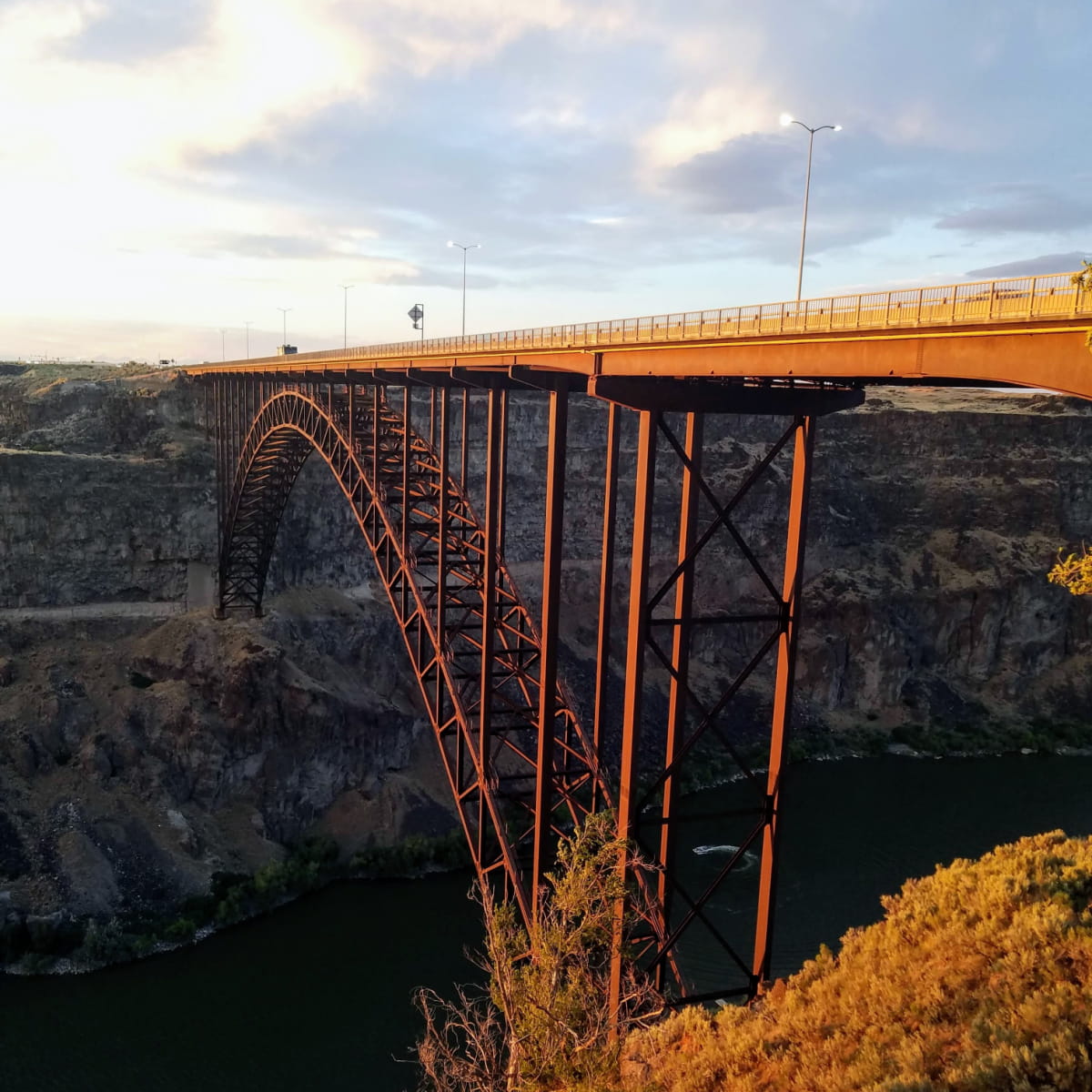 Arched bridge spanning a large canyon, metalwork reflecting in sunset.