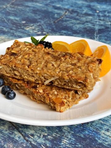 Two baked oatmeal breakfast bars on a plate with orange slices and fresh berries.