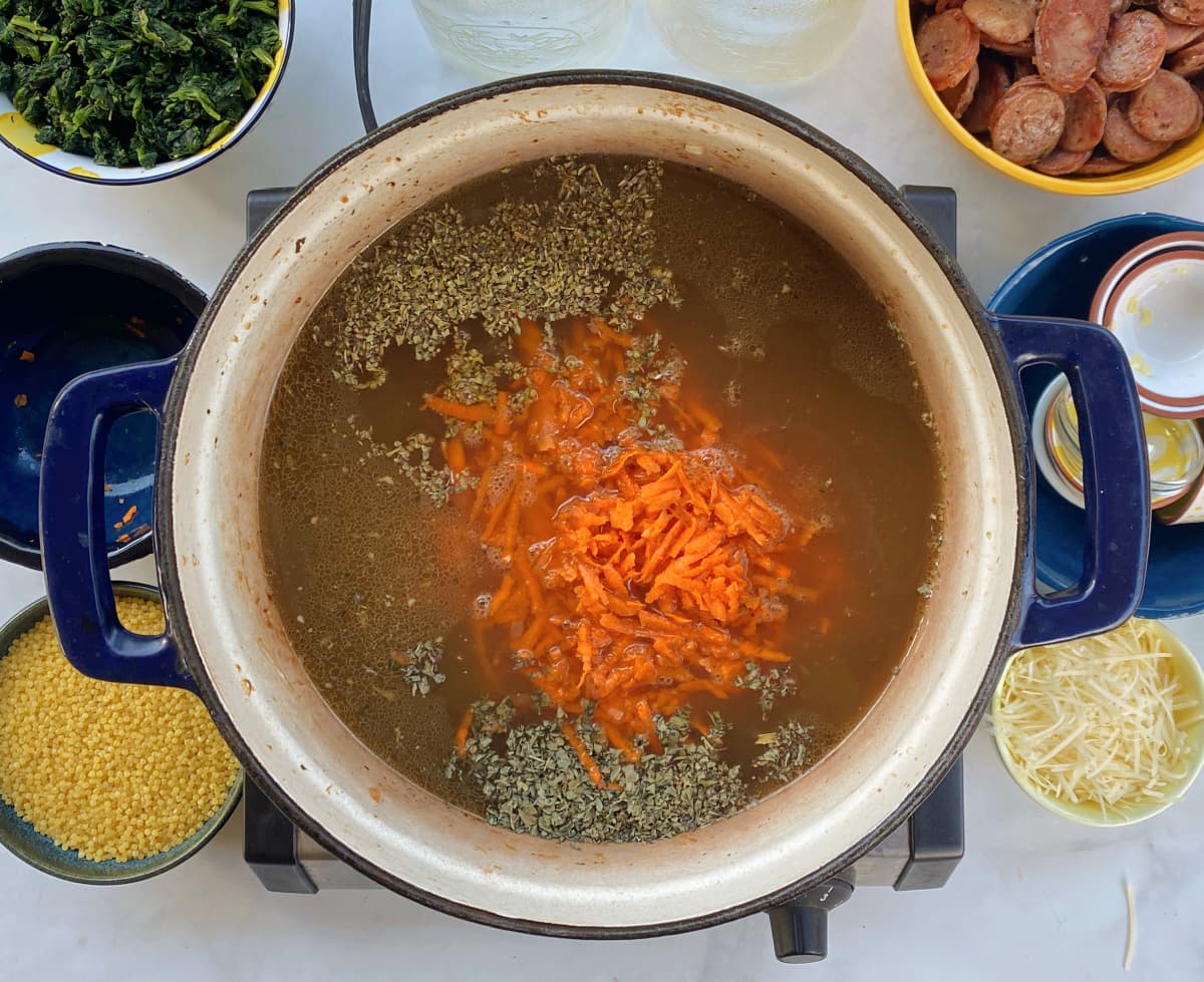 Chicken broth, carrots, herbs, and seasonings added to soup in Dutch oven.