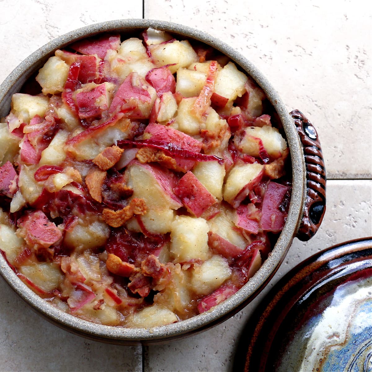 Red potatoes, red onions, bacon and other ingredients in a crockery casserole dish. 