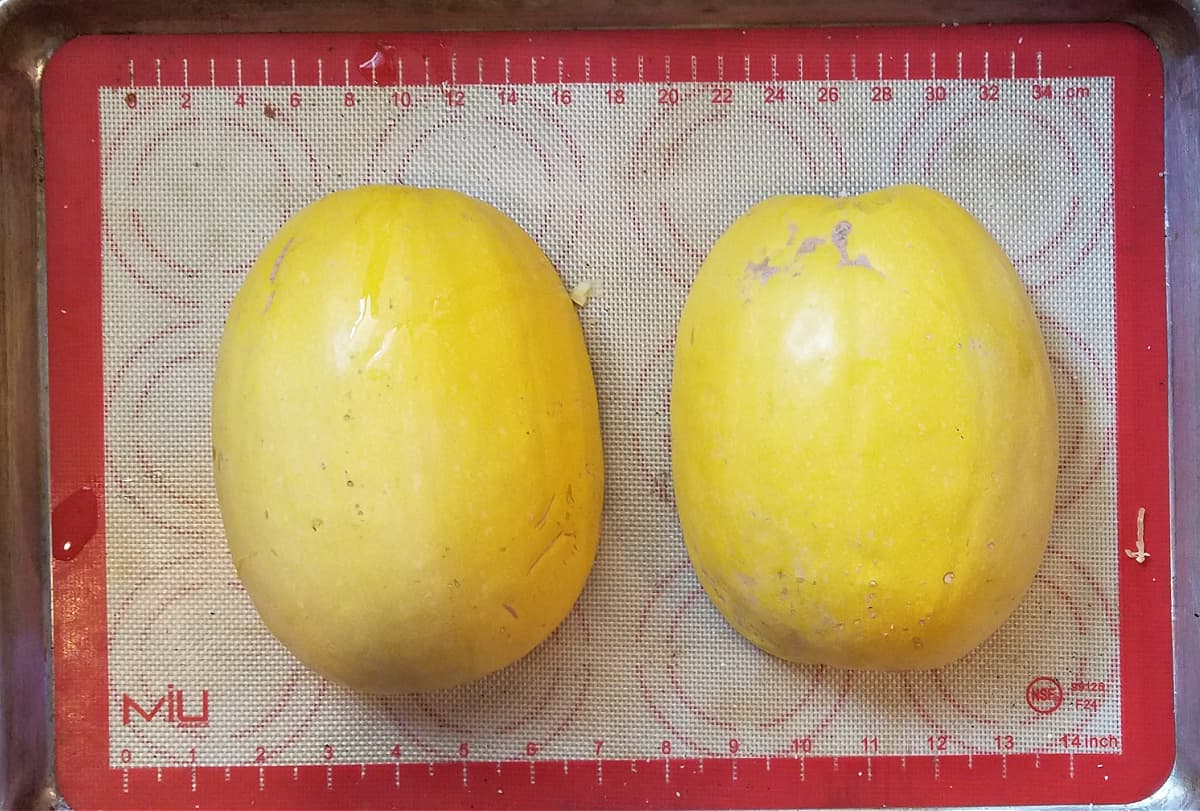 Spaghetti squash halves with cavities down on tray.
