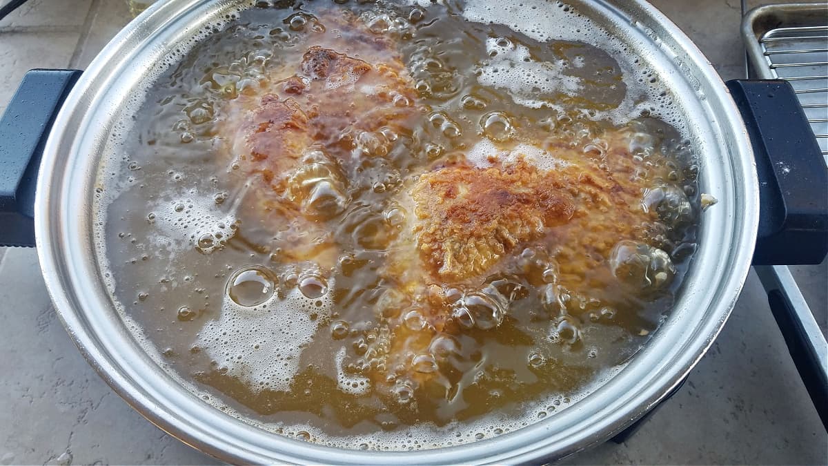 Two chicken quarters frying in an electric skillet.