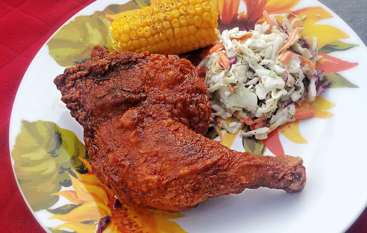 Fried chicken plated with coleslaw and corn on the cob.