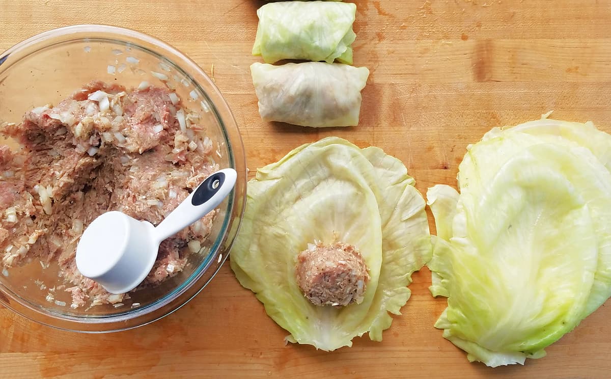 Mixing bowl filled with cabbage roll filling mix, a cabbage leaf with a small amount of filling int he center, and empty cabbage leaves.