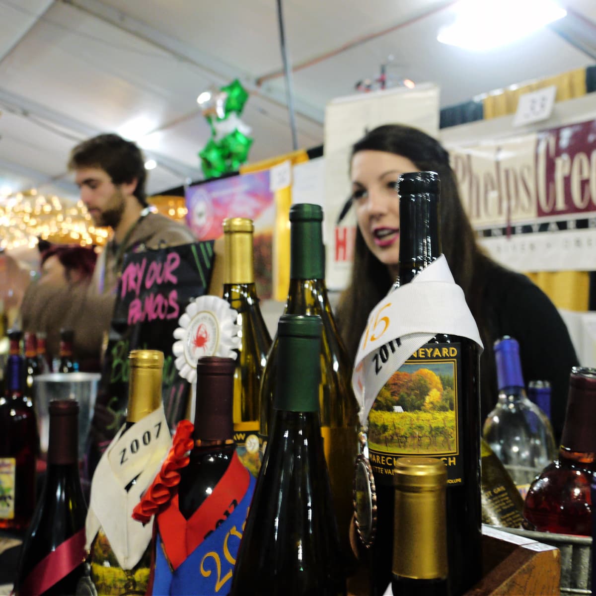 Young womand beind counter lined with wine bottles and wine awards. 