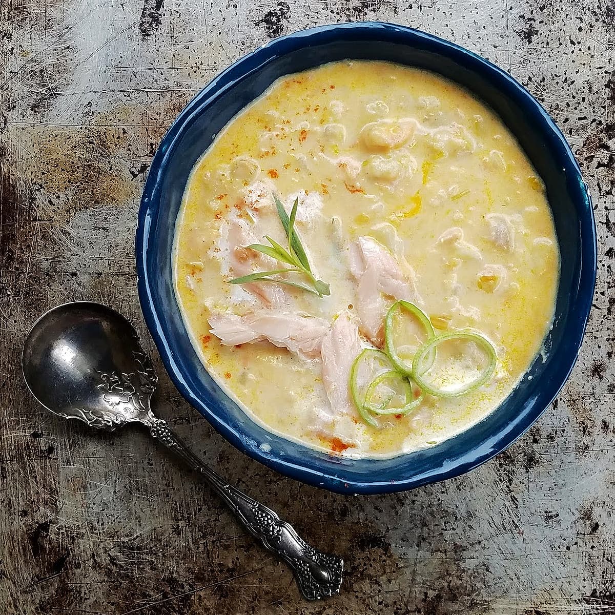 Bowl of salmon chowder, garnished with  flaked smoked salmon, leek rings, and a sprig of fresh tarragon. 