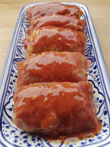 Cooked cabbage rolls lined up on a long serve tray, covered with sauce.