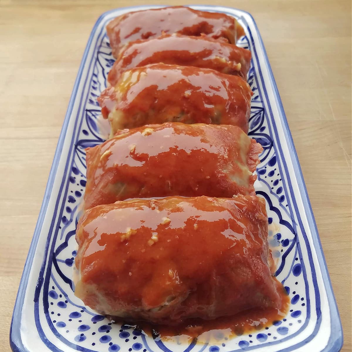Cooked cabbage rolls lined up on a long serve tray, covered with sauce. 