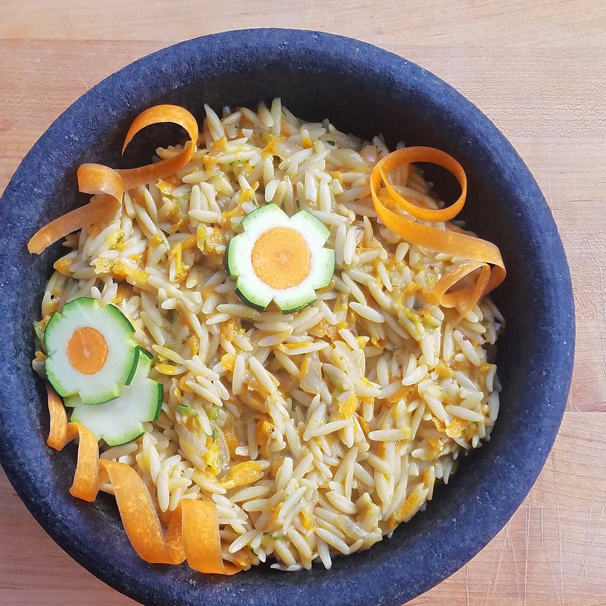 Cooked orzo in a stone bowl, garnished with zucchini-carrot flowers and carrot curls. 