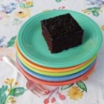 Single square of chocolate cake on a stack of old-fashioned plates.