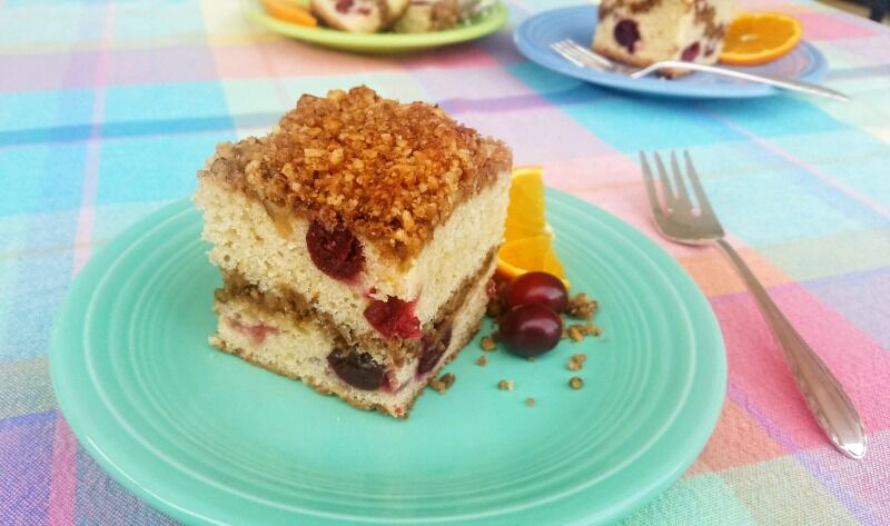 Coffee cake plated with cranberries and orange slices. Fork to the side. 