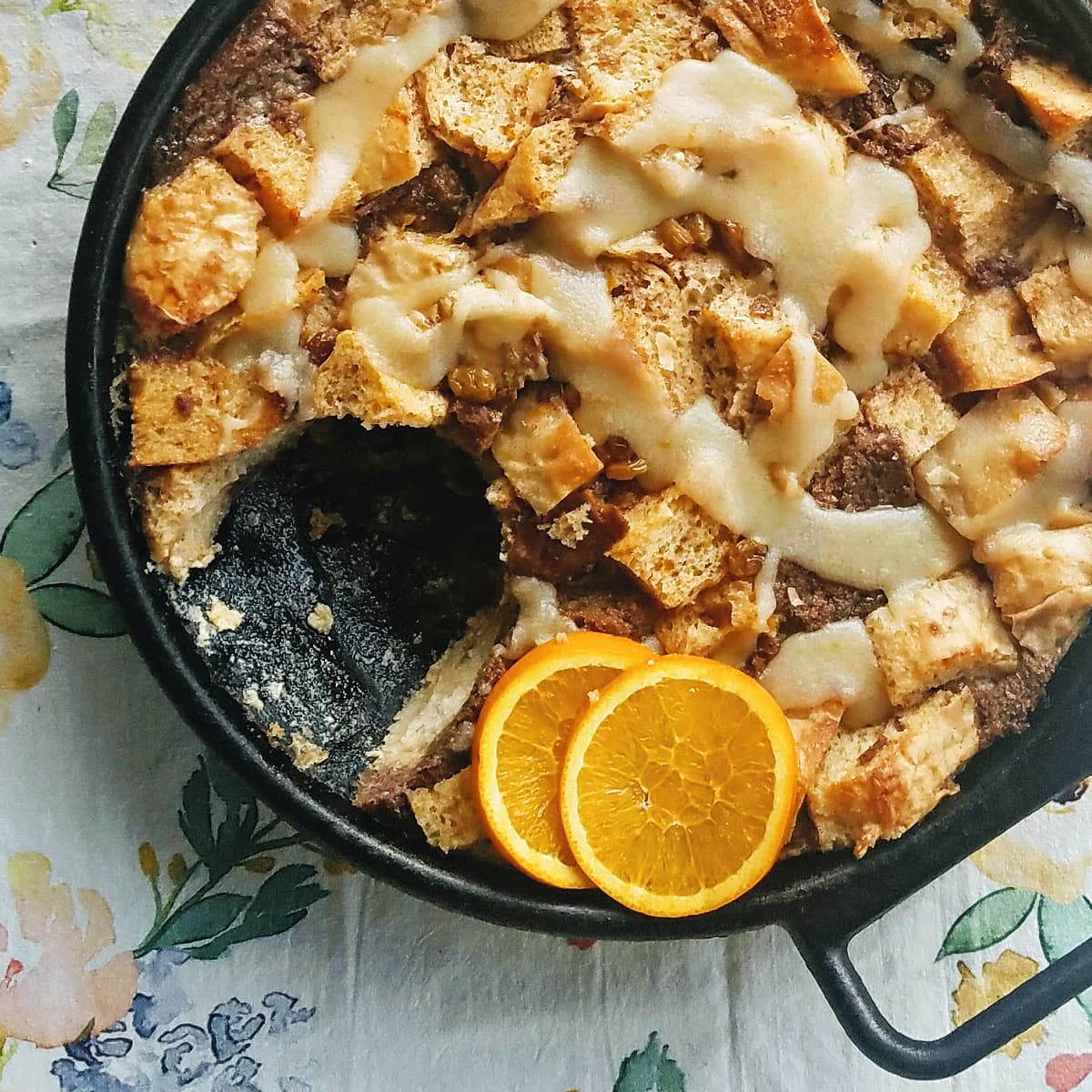 Bread pudding in a cast iron skillet, garnished with orange slices, with one serving removed.