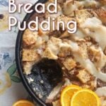 Over head of bread pudding with butter sauce, garnished with orange slices. In a cast iron skillet. Pin text reads: Classic Bread Pudding with whiskey sauce.