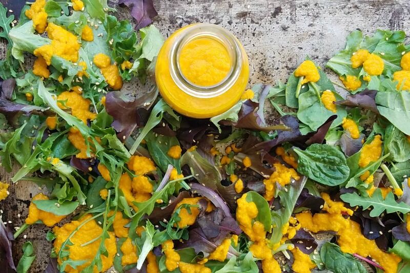 Bottle of Carrot Ginger Dressing on a tray with dressed greens. 