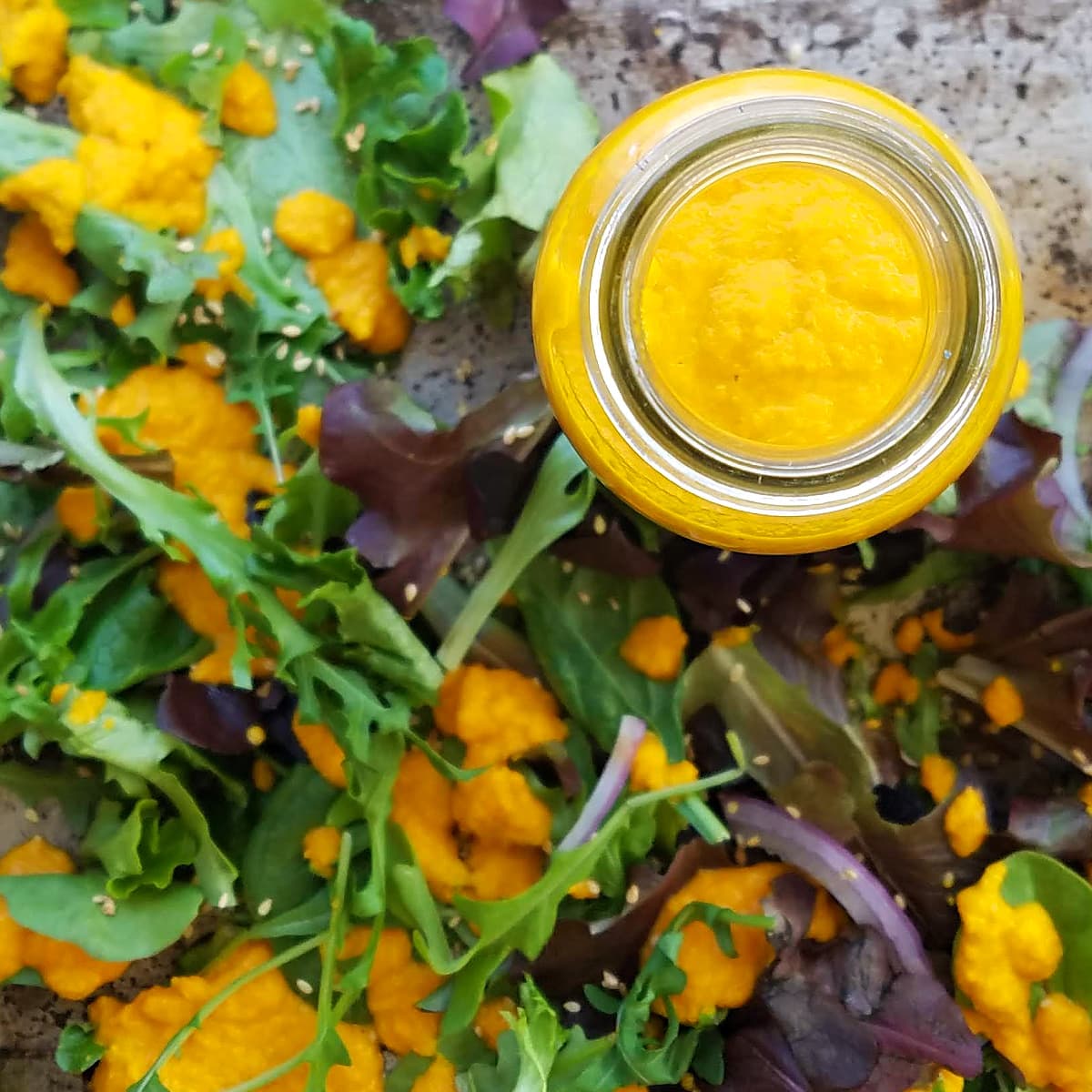 Overhead shot of a bottle of Carrot Ginger Dressing on a tray with dressed greens. 