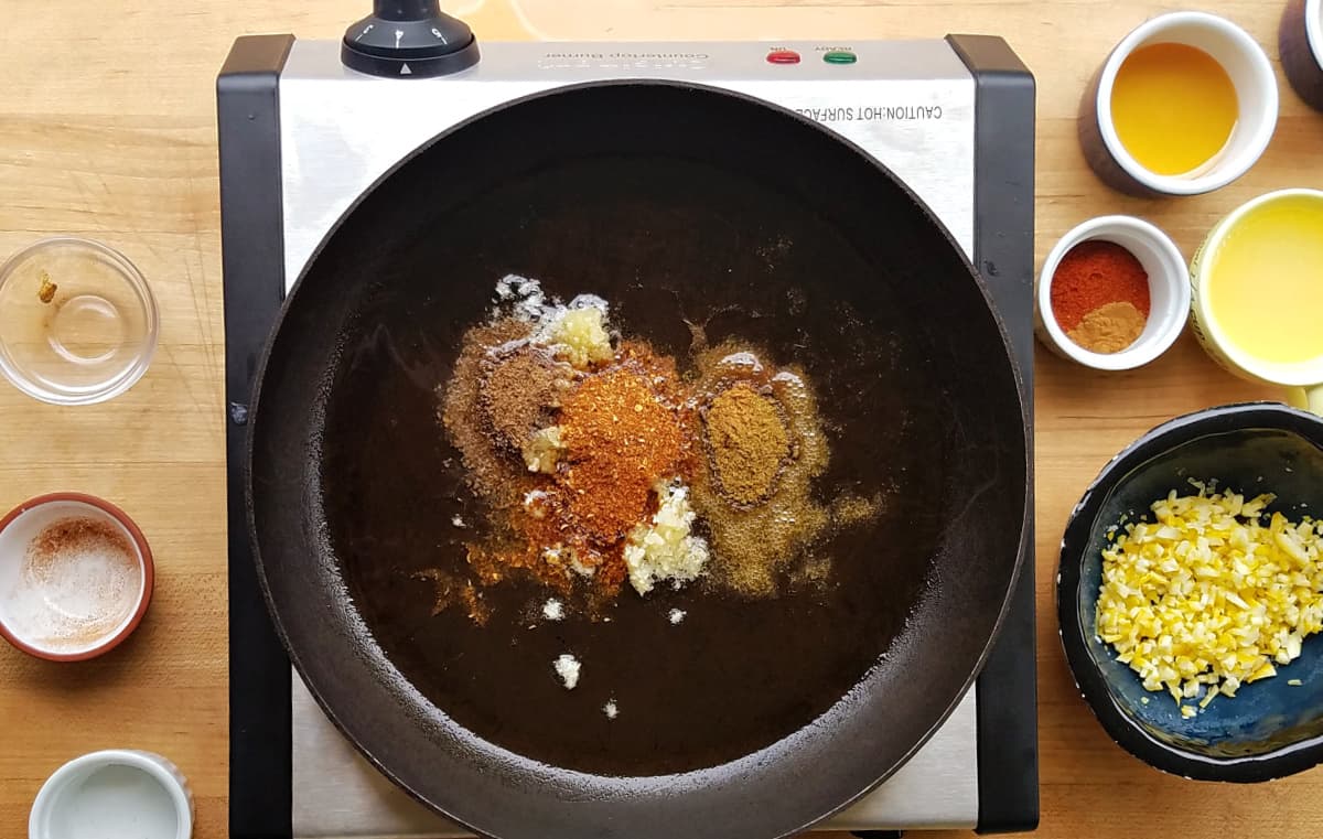 Spices and oil in small frying pan, unmixed.